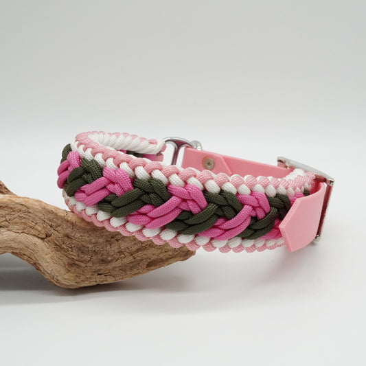Ein geflochtenes Hundehalsband in den Farben Pink, Grün und Weiß liegt auf einem Stück Treibholz. Das Halsband hat eine pinkfarbene Schnalle und ist aus Paracord gefertigt.